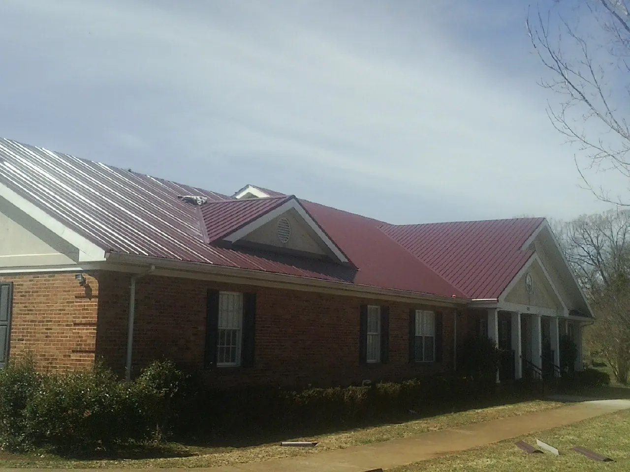 Red metal roof with gabled entries on a long brick building, from a Hail Damage Roof Repair job in Houtzdale