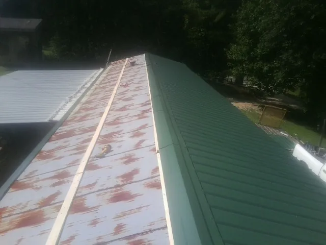 Old rusted panels beside newly installed green metal roofing — Wind Damage Roof Repair by Roofing Brothers in Houtzdale