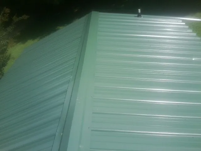New green metal panels meeting at the ridge of a roof — Flat Roof Repair work by our crew in Houtzdale