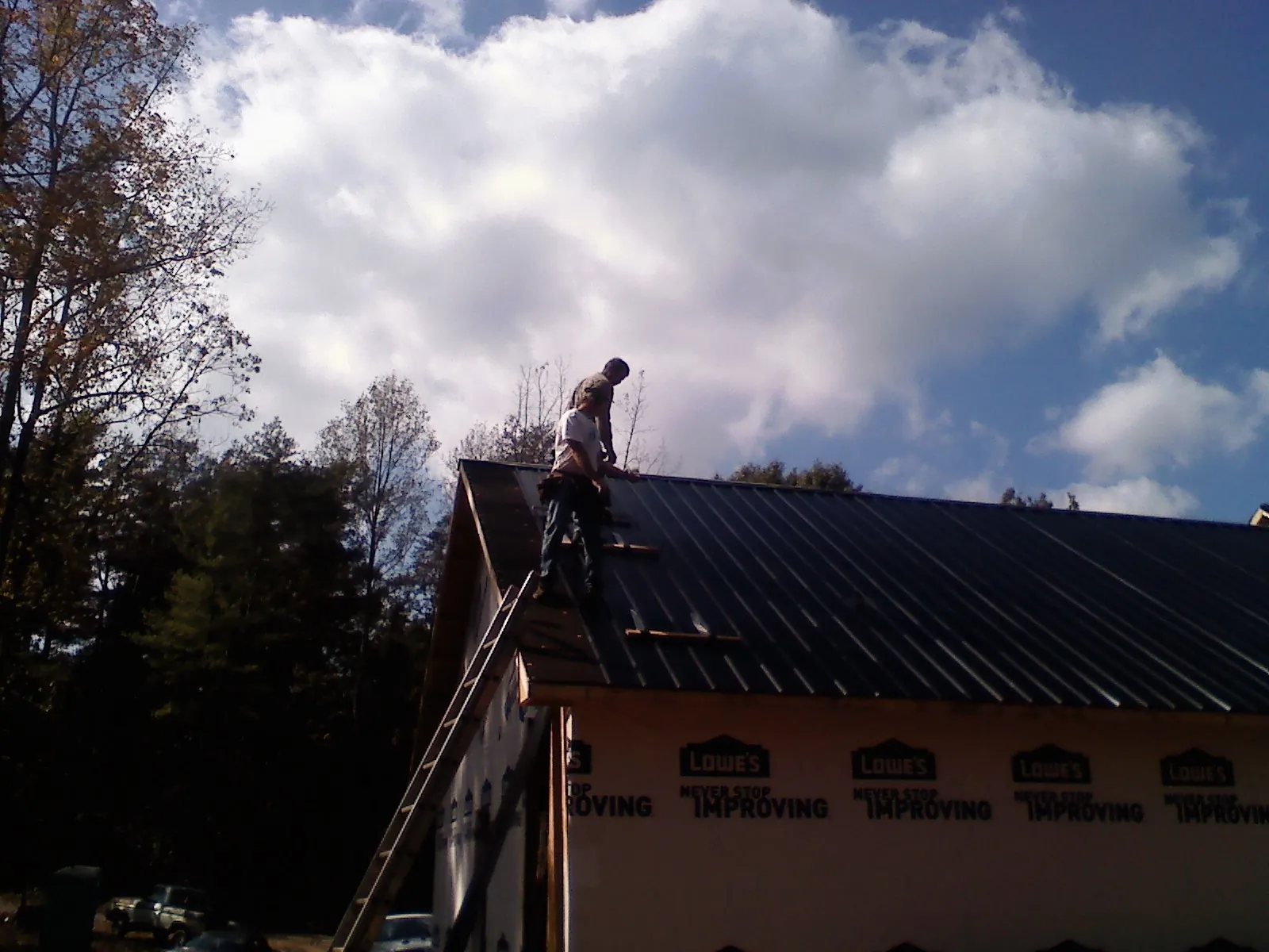 Roofer fastening dark metal panels high against a cloudy sky, from a Roof Inspection job in Houtzdale