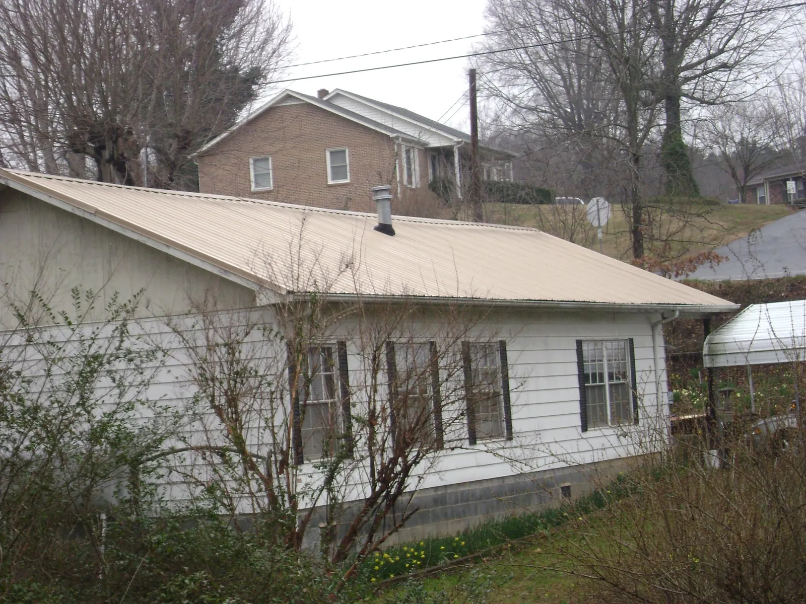 Tan metal roof on a white sided house set into a hillside — Commercial Roofing by Roofing Brothers in Houtzdale